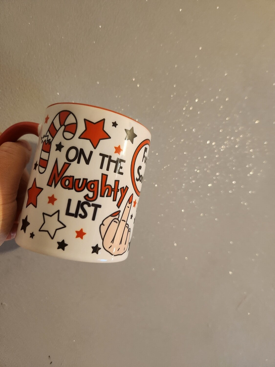 Mug with 'On the Naughty List' text and festive design held against a sparkly background